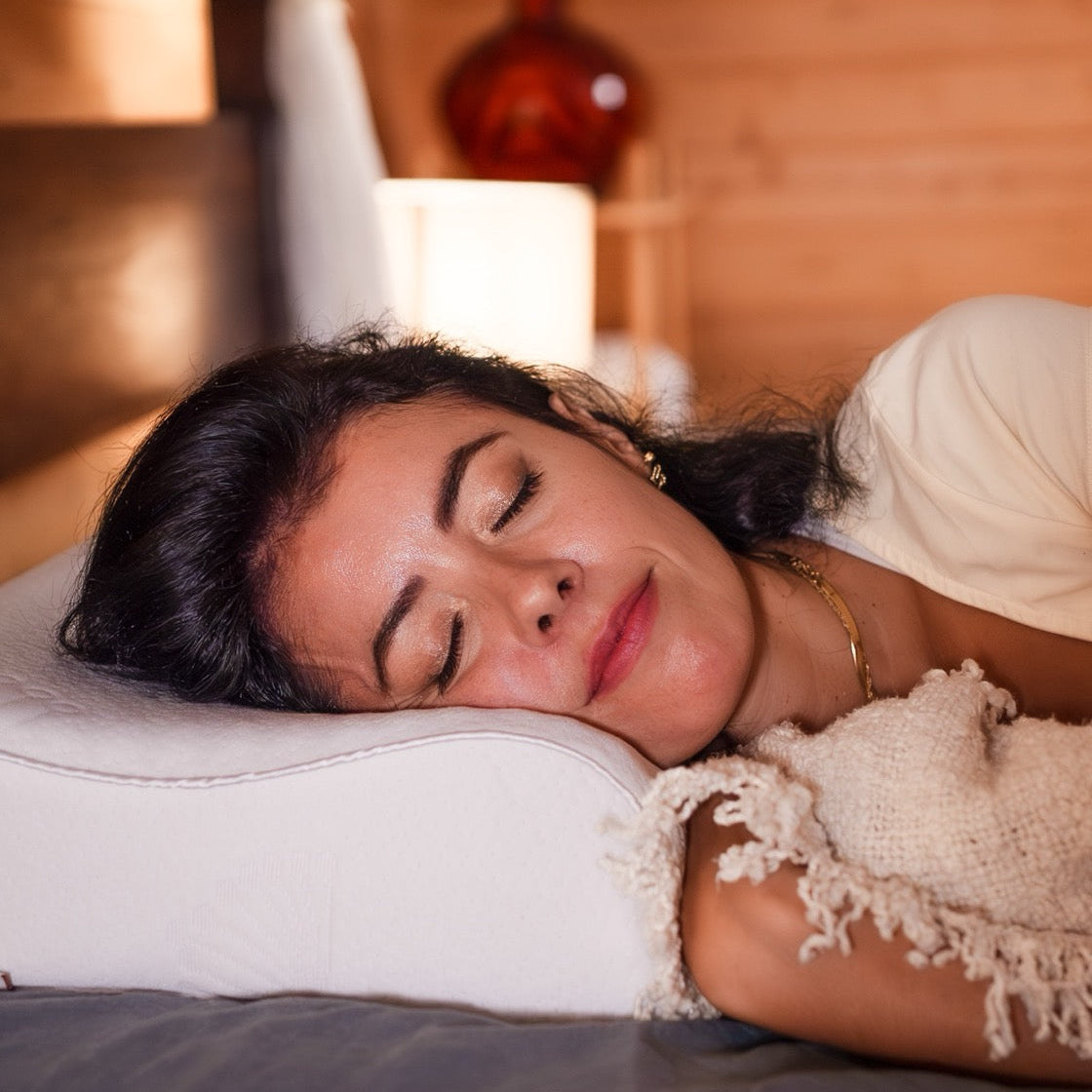 A woman rests her head on a posture form contoured pillow on a bed, the pillow adjust to her sleeping position and she looks very comfortable